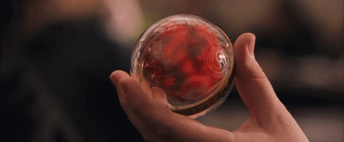 A hand holding a transparent ball filled with red smoke